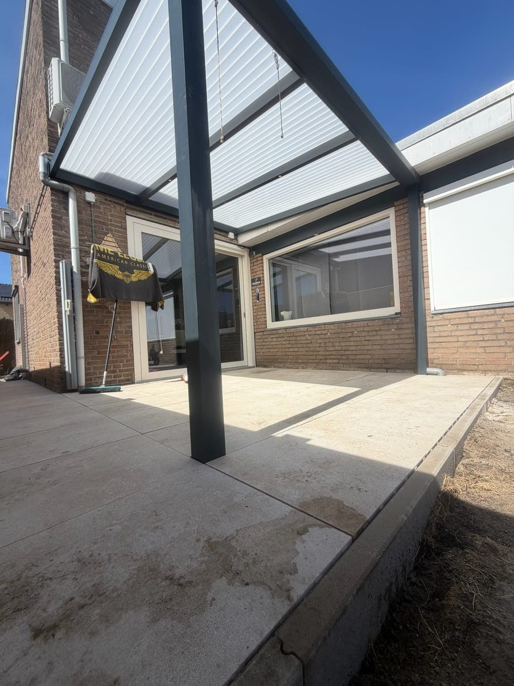 Het nieuwe terras van lichte betontegels onder de overkapping, met de opsluitband langs de rand van het zandbed.
