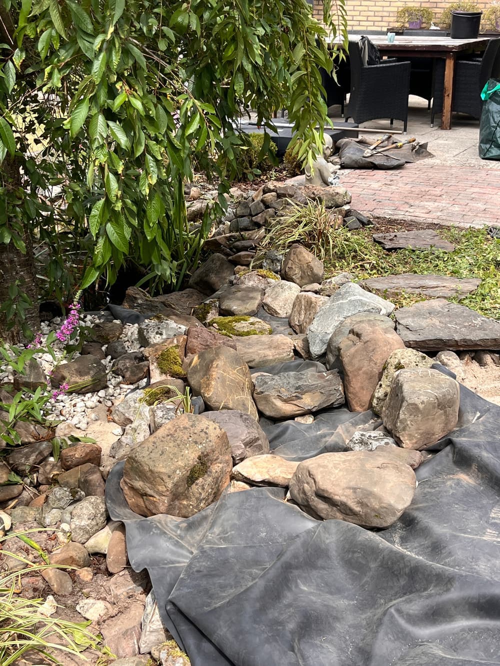 Keien en natuursteen op de vijverfolie aan de rand bij het terras, waar het water overgaat in de tuin.
