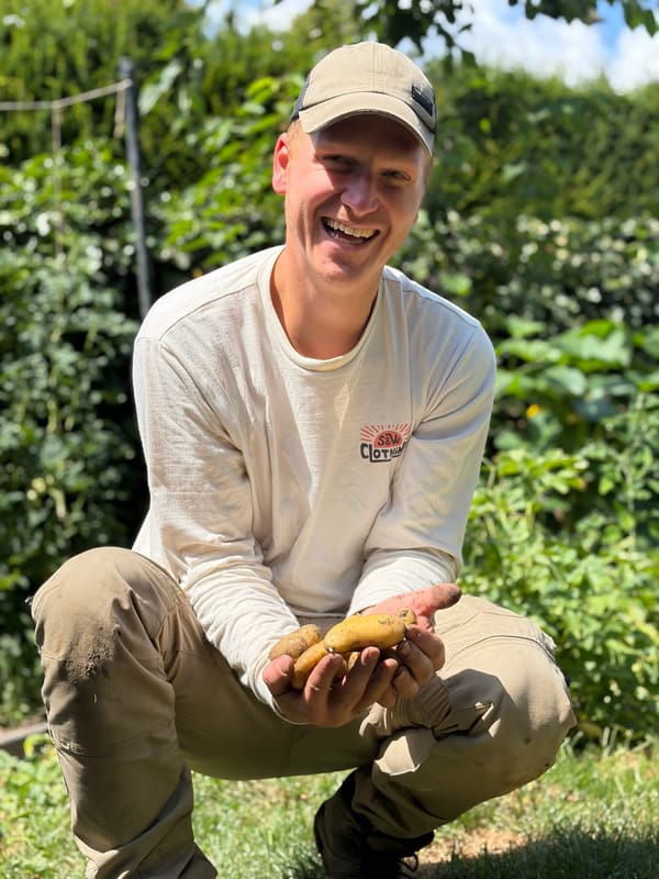 Nick gehurkt in de moestuin, lachend, met een handvol pas gerooide aardappels.